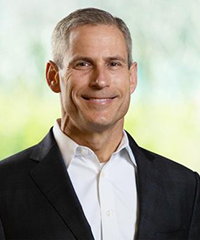 A headshot of Dana Jackson in a black blazer and white dress shirt